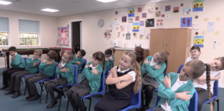 Building secure attachments in the wake of Covid-19 A class of children, all crossing their arms, doing an exercise that promotes good attachment
