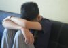 Representing those with SEND in court A teen boy with his head in his arms, wearing a shirt that says 'NYPD'