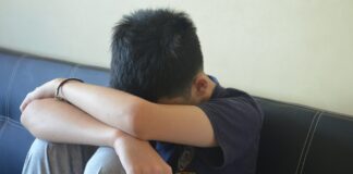 Representing those with SEND in court A teen boy with his head in his arms, wearing a shirt that says 'NYPD'
