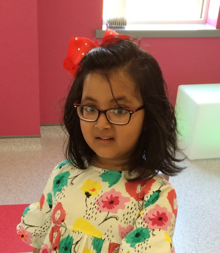 A young girl who has Bardet-Biedl syndrome. She has black hair and a pink bow in her hair