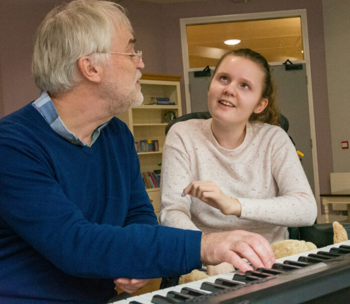 Adam and Lily Dr Adam Ockleford, a man with gray hair and a blue jumper, plays the piano for Lily, who has juvenile dementia and is wearing a pink jumper