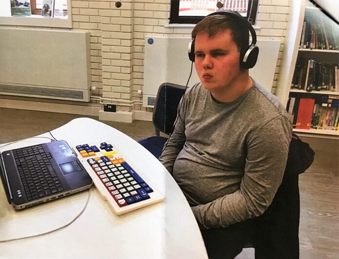 Ben 2 (2) A photo of Ben, a young adult with BBS, sitting at a computer wearing headphones