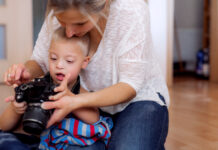 The future of Down’s Syndrome therapy is just around the corner A handicapped down syndrome boy and his mother with a digital camera indoors, taking pictures.