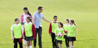 Learning outside the classroom in unprecedented times Group of school children wearing bibs and school uniform outside on the grass with their teacher. One of the boys is holding a soccor ball.