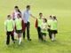 Learning outside the classroom in unprecedented times Group of school children wearing bibs and school uniform outside on the grass with their teacher. One of the boys is holding a soccor ball.