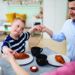 Happy down syndrome boy with parents at the table, praying before breakfast.